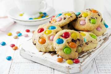 Stack of children's cookies with colorful chocolate candies in a sugar glaze on a white light wooden background. Selective focus