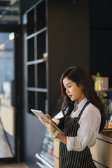 Portrait of a smiling Asian entrepreneur standing behind her cafe counter using a digital tablet.