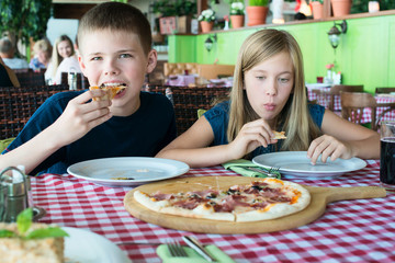 Obraz na płótnie Canvas Happy teenagers eating pizza in a cafe. Friends or siblings having fun in restaurant.