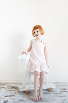 Red-haired girl in a pink dress is sitting on a toy horse