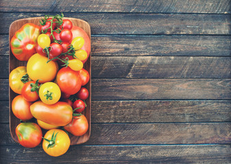 Colorful Organic Tomatoes in wooden plate with copy space. Fresh Red Yellow Orange and Green Tomatoes on wooden background. Retro styled.