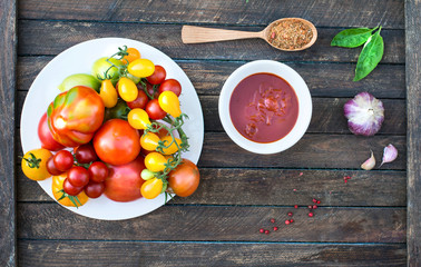 Colorful Organic Tomatoes in white plate with ketchup spices and basil. Fresh Red Yellow Orange and Green Tomatoes on wooden background with copyspace. Ketchup making concept.