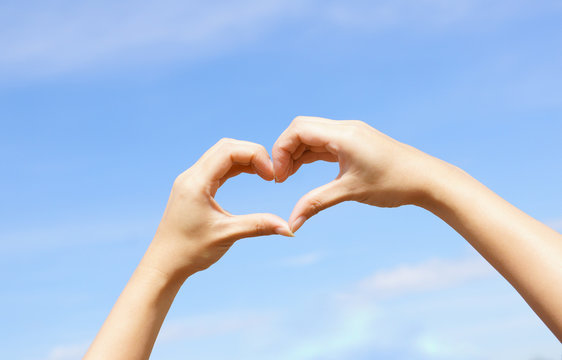 Hands forming a heart shape with blue sky background