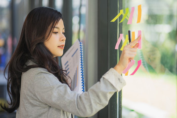 Business plan. Young female professional sticking colourful notes to a glass wall