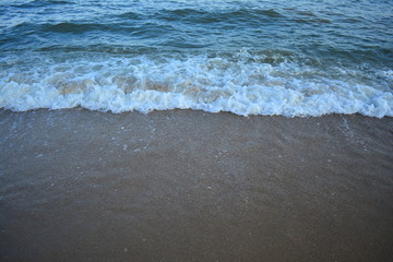 Hard wave of blue ocean on sandy beach background in last sun light