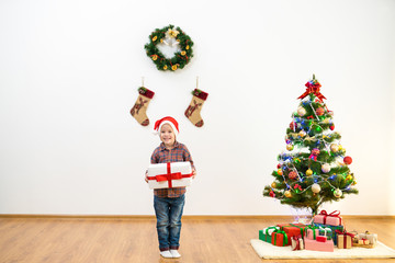 The happy boy stand near the christmas tree and hold a gift box
