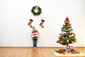 The happy boy stand near the christmas tree and hold a gift box