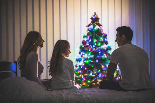 The happy family sit on the bed near the christmas tree