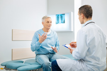 Health problems. Nice pleasant elderly man sitting on the bed and gesticulating while telling the...
