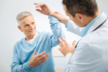Fototapeta premium Caring about health. Nice cheerful senior man looking at his therapist and raising his hand up while smiling