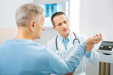 Fototapeta premium Professional physician. Smart nice professional therapist looking at the patients hand and thinking about diagnosis while doing a checkup