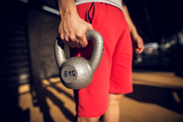 Close up side view of man's hand holding the 8kg kettlebell in the sunny garage.