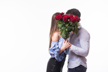 Portrait of a young lovely couple kissing while standing and holding flower bouquet over white background