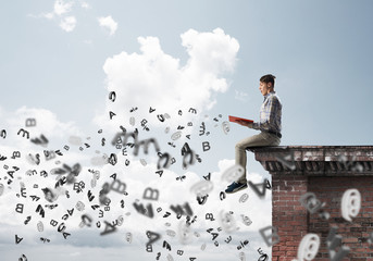 Man on roof edge reading book and symbols flying around