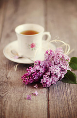 Fototapeta na wymiar Tazza di tè su tavolo in legno con fiori di lillà. Immagine romantica