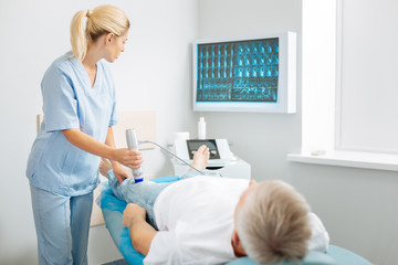 Obraz premium Ultrasound scanning. Nice professional pleasant doctor looking at the screen and putting a diagnosis while doing ultrasound scanning