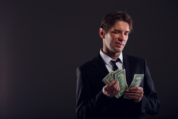 Image of man in suit counting dollars isolated on black background.