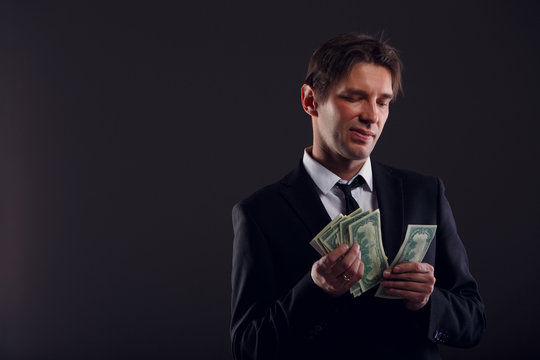 Image of man in suit counting dollars isolated on black background.