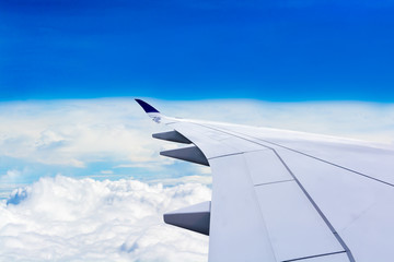 Obraz premium The wing looks out of the plane window. While flying over the white clouds and overlooking the horizon and blue sky. Free space for text and more.