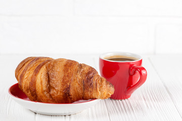 Freshly baked croissant on napkin, cup of coffee in red cup on white wooden background. French breakfast. Fresh pastries for breakfast. Delicious dessert. Closeup photography. Horizontal banner