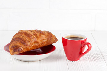 Freshly baked croissant on napkin, cup of coffee in red cup on white wooden background. French breakfast. Fresh pastries for breakfast. Delicious dessert. Closeup photography. Horizontal banner