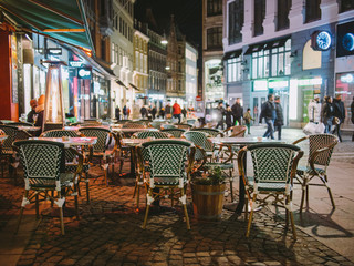 Fototapeta na wymiar Public outdoor restaurant in the streets of Copenhagen at night with neon lights and vintage chairs