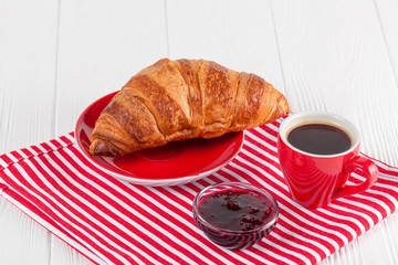 Freshly baked croissant on napkin, cup of coffee in red cup on white wooden background. French breakfast. Fresh pastries for breakfast. Delicious dessert. Closeup photography. Horizontal banner