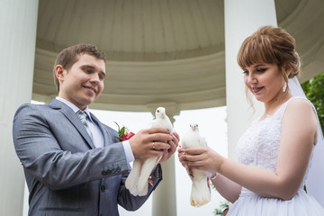 Bride and groom near the white columns and the pigeons in their hands