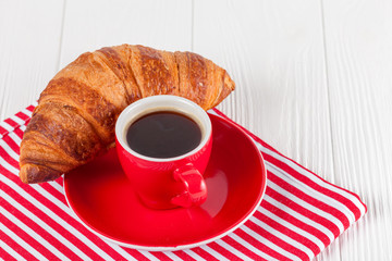 Freshly baked croissant on napkin, cup of coffee in red cup on white wooden background. French breakfast. Fresh pastries for breakfast. Delicious dessert. Closeup photography. Horizontal banner
