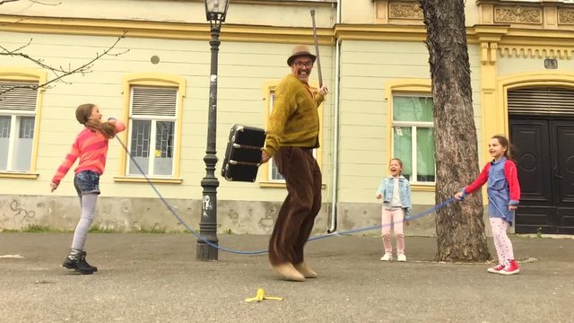 Old man jumping on a skipping rope with three girls in the street.
