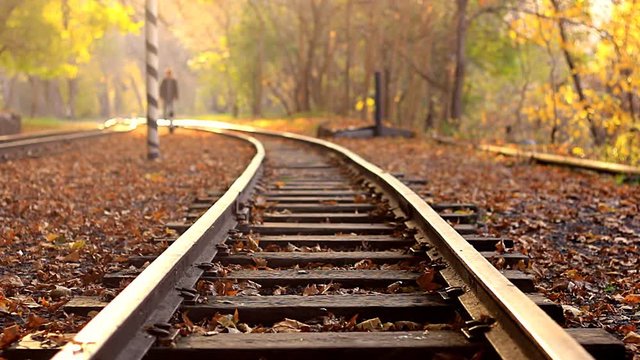 A man walks down train tracks on a background golden Autumn forest. A man approaches the camera
