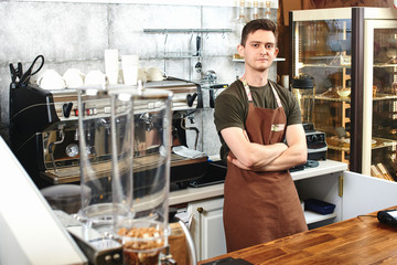 The portrait of the guy baristas at workplace on background of coffee