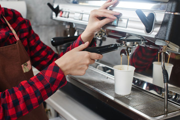 Girl Barista in the red shirt makes the coffee. Close-up of hands