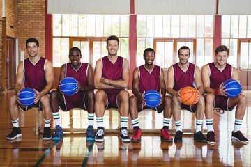 Smiling basketball players sitting on bench with basketball in