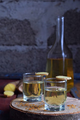 Homemade ginger tincture or ale on wooden background. Rustic style. Spice yellow liqueur in a glass. Alcohol drink.