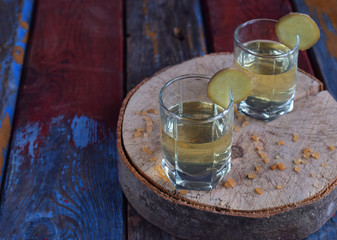 Homemade ginger tincture or ale on wooden background. Rustic style. Spice yellow liqueur in a glass. Alcohol drink.