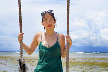 happy Asian Chinese woman holding swing rope having fun isolated on a Summer blue sky smiling positive and cheerful in holidays