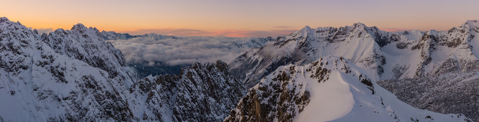 Panoramic view of a winter sunset in the Alps with a layer of cloouds in the valley and a lot of snow on the mountains.