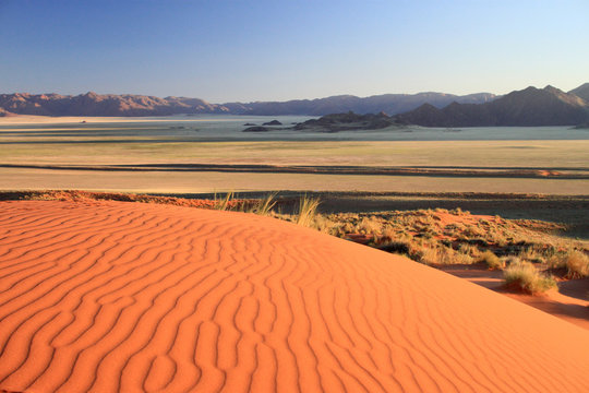 Sandd&uuml;ne der Namibw&uuml;ster im Vordergrund, gr&uuml;nliche Ebene im Mittelgrund und Tiras-Berge im Hintergrund.Where: Farm GUnsbewys bei Aus, D707, Namibia.