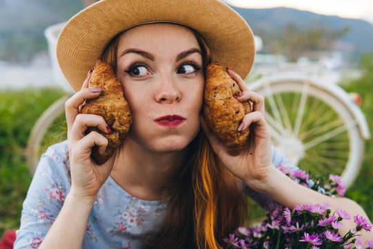 Funny woman with croissants and flowers, enjoying picnic