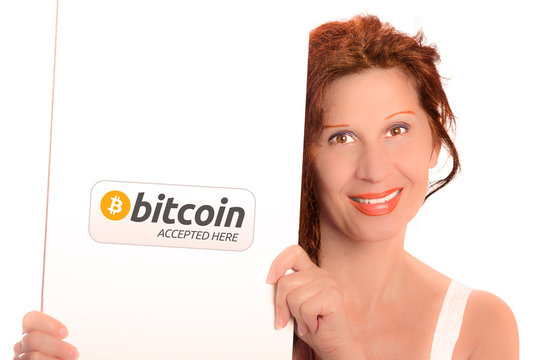 Happy woman with Arab and Middle Eastern somatic traits and long red hair smiles holding  white signboard in portrait orientation with Bitcoin Accepted Here public domain logo
