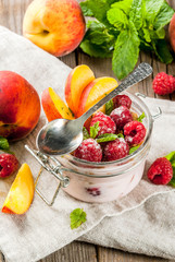 Summer healthy breakfast. Overnight oatmeal in a jar, granola, nuts, fresh raspberries and peach, decorated with mint leaves. On the old rustic wooden table. Copy space