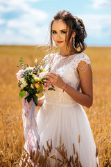 Fototapeta na wymiar Portrait of beautiful bride with wedding bouquet in hands and looking at camera, outdoors In a field of wheat