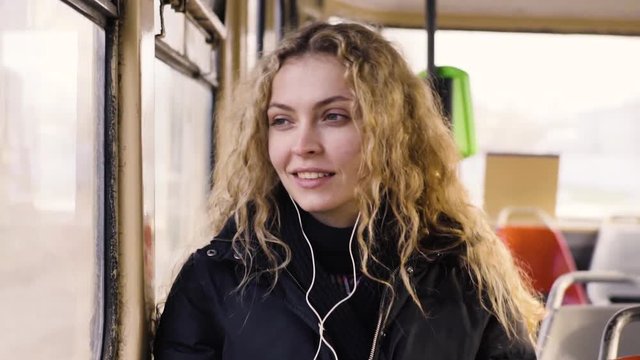 Pretty woman listening music in headphones on smartphone riding tram