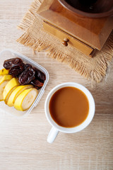 Fototapeta na wymiar Bananas and dates in the container, and a cup of coffee with milk, on a wooden table.
