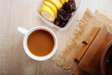 Bananas and dates in the container, and a cup of coffee with milk, on a wooden table.