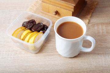 Bananas and dates in the container, and a cup of coffee with milk, on a wooden table.