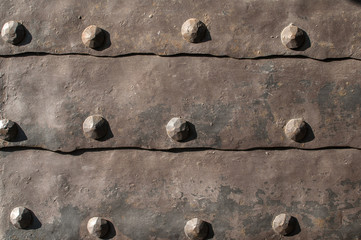 Detail of old medieval door with metal cladding surface and iron rivets closeup as background
