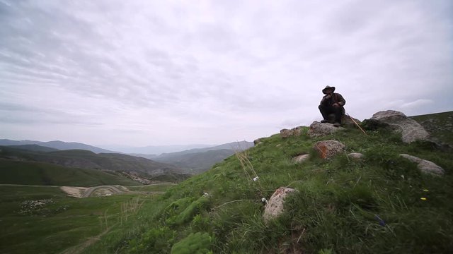 Man seated on top of the mountain observing the fields