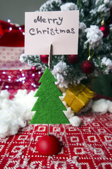 Fototapeta na wymiar paper with the inscription Merry Christmas attached to a toy tree. New Year's mess on the background